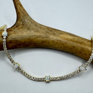 May include: A gold chain bracelet with a row of small clear stones and four larger white opal stones.