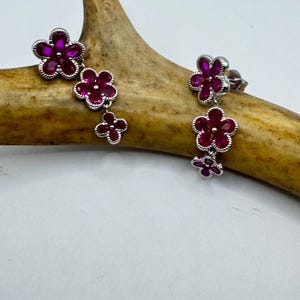 May include: A pair of dangle earrings featuring a cluster of ruby red flowers. The earrings are made of silver and have a polished finish.