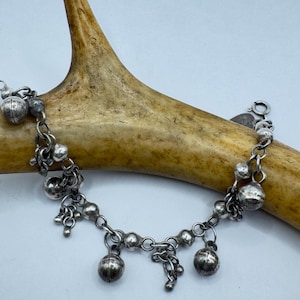 Puede incluir: Un brazalete de plata con múltiples dijes redondos y un cierre de langosta.