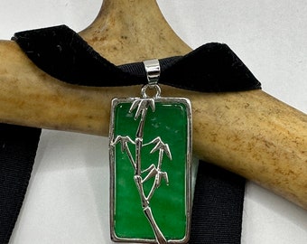 May include: A silver pendant necklace with a green jade stone featuring a silver bamboo design. The necklace is on a black velvet ribbon.