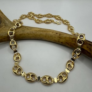 May include: A gold chain necklace with a mariner link design. The chain is made of polished gold and has a lobster clasp closure.