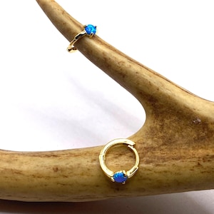 May include: A pair of gold hoop earrings with a small blue opal stone set in each hoop.