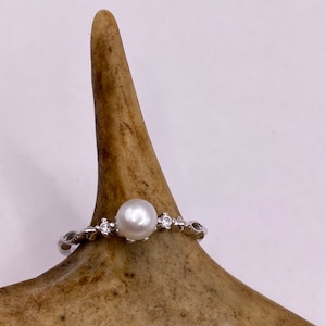 May include: A silver ring with a white pearl and small clear stones set in a delicate band.