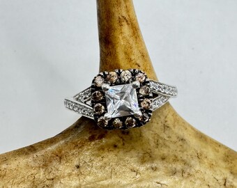 May include: A silver ring with a square-shaped clear center stone surrounded by a halo of smaller brown stones.