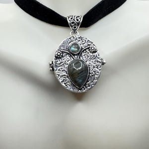 Puede incluir: Un collar de plata con un choker de terciopelo negro. El medall&oacute;n es de forma ovalada y presenta un intrincado dise&ntilde;o floral. El medall&oacute;n tiene una gran piedra preciosa de labradorita en forma de l&aacute;grima en el centro y una piedra preciosa redonda de labradorita m&aacute;s peque&ntilde;a encima.