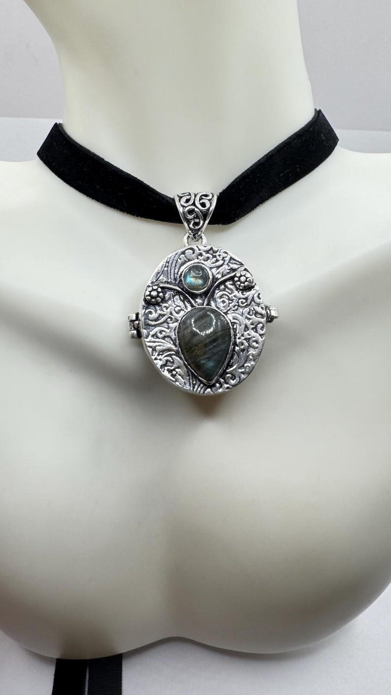 Puede incluir: Un collar de plata con un choker de terciopelo negro. El medall&oacute;n es de forma ovalada y presenta un intrincado dise&ntilde;o floral. El medall&oacute;n tiene una gran piedra preciosa de labradorita en forma de l&aacute;grima en el centro y una piedra preciosa redonda de labradorita m&aacute;s peque&ntilde;a encima.