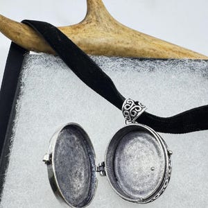 Puede incluir: Un collar con un medall&oacute;n de plata con un dise&ntilde;o ornamentado. El medall&oacute;n est&aacute; abierto, revelando un interior vac&iacute;o.