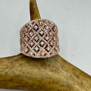 May include: A wide rose gold band ring with a diamond lattice design. The ring is set on a brown antler.