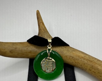 May include: A green jade pendant with a gold Chinese character for "good fortune" hanging on a black velvet ribbon.