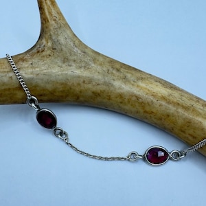 May include: A silver chain bracelet with two oval-shaped red gemstones.