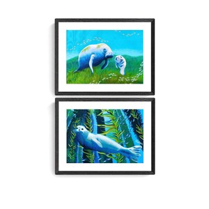 May include: Two framed paintings of marine life. The top painting shows a mother and baby manatee swimming in blue water with green seaweed. The bottom painting shows a seal swimming in blue water with green kelp.