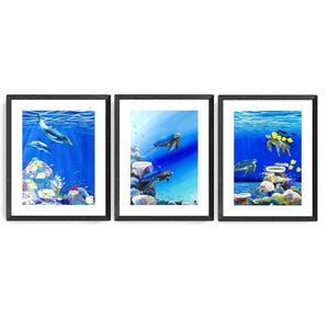 May include: Three framed paintings depicting underwater scenes. The first painting shows two dolphins swimming in a blue ocean with coral reefs. The second painting shows a sea turtle swimming in a blue ocean with coral reefs. The third painting shows a group of sea turtles swimming in a blue ocean with coral reefs.