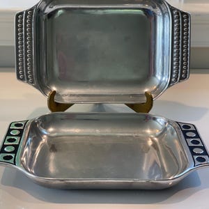 Könnte beinhalten: Zwei silberne Servierplatten mit schwarzen und weißen geometrischen Mustern. Die größere Platte hat einen perlenbesetzten Rand. Die kleinere Platte hat ein geometrisches Muster an den Griffen.