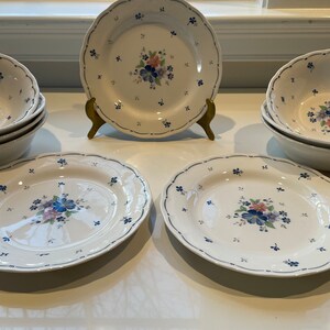 Puede incluir: Juego de platos y cuencos de cerámica blanca con un diseño azul y floral. Los platos y los cuencos tienen un borde festoneado y un ribete azul.