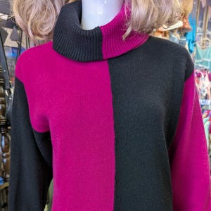 May include: A long-sleeved, color-blocked sweater in black and magenta. The sweater features a turtleneck and a checkerboard design, with the colors alternating in large squares. The garment is displayed on a mannequin.