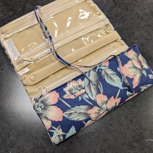 May include: A blue and pink floral print jewelry roll with clear plastic pockets and a zipper closure. The roll is open and the pockets are visible.