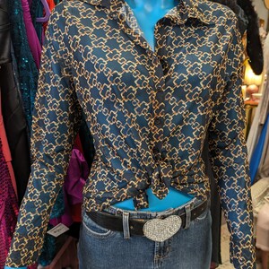 May include: A long-sleeved, blue and gold patterned blouse with a button-up front and a tied knot at the waist. The blouse is worn with a black belt and a heart-shaped rhinestone buckle.