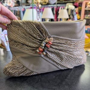 Puede incluir: Bot&iacute;n color topo con una superposici&oacute;n de tela estampada y una parte superior de cuero. El bot&iacute;n presenta un acento decorativo de cuentas en tonos naranja, beige y gris. El bot&iacute;n se exhibe sobre una superficie oscura.