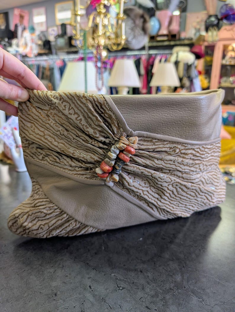 Puede incluir: Bot&iacute;n color topo con una superposici&oacute;n de tela estampada y una parte superior de cuero. El bot&iacute;n presenta un acento decorativo de cuentas en tonos naranja, beige y gris. El bot&iacute;n se exhibe sobre una superficie oscura.