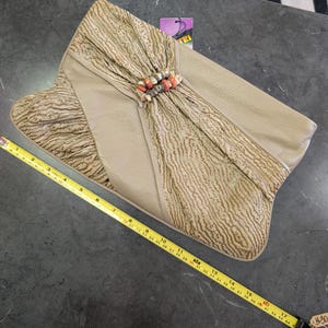 Puede incluir: Bolso de mano beige con solapa texturizada y un acento decorativo de cuentas. El bolso de mano mide aproximadamente 43 cm de largo. La bolsa tiene una etiqueta que dice "TRI".