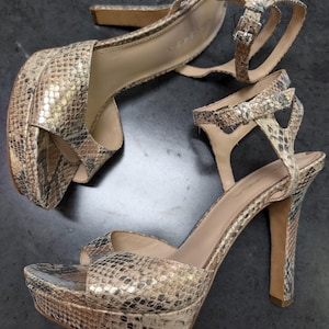 May include: A pair of high-heeled sandals with a snakeskin pattern. The sandals have a platform and an ankle strap.