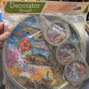 May include: A set of six gold-rimmed coasters featuring a map of Florida with various landmarks and the text "Decorator Styled".