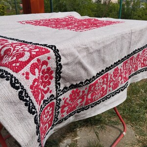 May include: A white tablecloth with a red and black embroidered floral design. The tablecloth is folded and draped over a red metal drying rack.
