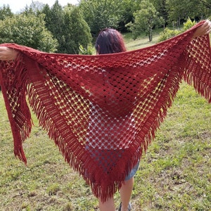 May include: A red crocheted shawl with fringe. The shawl is made with a delicate openwork pattern.