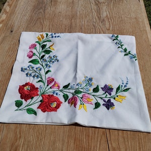 Peut inclure: Taie d'oreiller blanche avec un motif floral brodé. Les fleurs sont rouges, roses, jaunes, bleues et violettes. Les feuilles sont vertes.