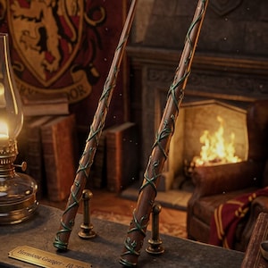 May include: Two brown wooden wands with green vine-like detailing wrapped around the shafts. Each wand stands on a small metal base with a plaque. The plaques read Hermione Granger - 10.75 inches and Hermione Granger - 14 inches respectively.