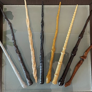 以下が含まれることがあります： それぞれユニークなデザインと色を持つ、10本の異なる木製の杖。杖はガラスの表面に一列に並んでいます。