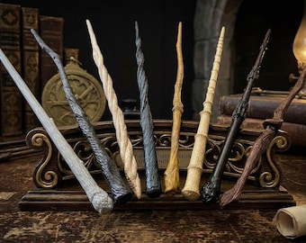 May include: A collection of eight distinct wands displayed in a decorative wooden stand. The wands feature varied textures and finishes, including light gray, dark charcoal, spiral-carved beige, black, natural wood grain, and dark brown wood tones.