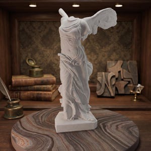 May include: A white matte sculpture of the Winged Victory of Samothrace, depicting a headless, winged figure in flowing, draped garments standing on a rectangular base. The statue features intricate folds in the fabric and outstretched wings.