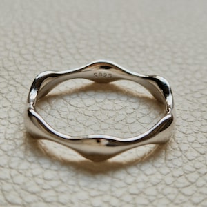 Op de afbeelding: Een zilverkleurige ring met een golvend ontwerp. De ring heeft een glad, gepolijst oppervlak en een minimalistische uitstraling. De ring is gemarkeerd met "S925".