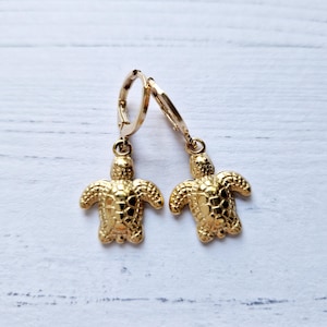 Op de afbeelding: Gouden turtle oorhangers met een getextureerde afwerking. De oorbellen hebben een hoepel sluiting.