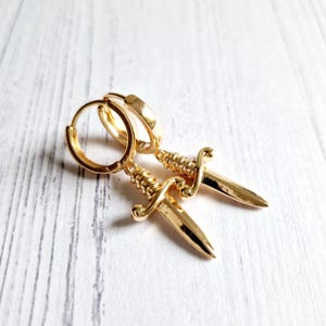 Op de afbeelding: Gouden creolen met een dolkbedel aan elke oorring.