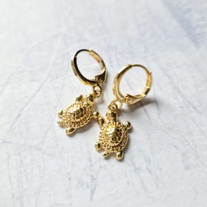 Op de afbeelding: Gouden creolen met een klein schildpadbedeltje dat aan elke creool hangt.