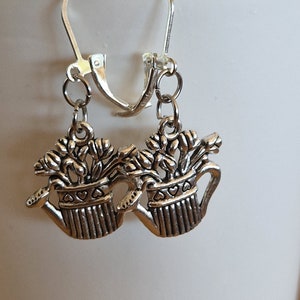 May include: Silver tone earrings featuring a pair of watering cans with flowers. The watering cans have a heart design on the side.