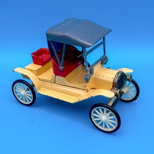 Könnte beinhalten: Ein gelbes Spielzeugauto mit einem grauen Stoffverdeck und roten Sitzen. Das Auto hat vier schwarze Räder und einen detaillierten Kühlergrill.