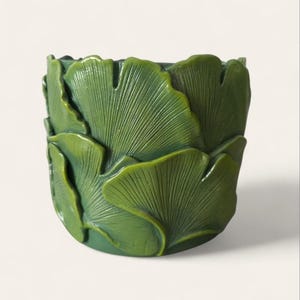 Peut inclure: Un pot de fleurs en céramique verte avec un motif détaillé de feuilles de ginkgo. Les feuilles sont superposées et texturées, créant un effet tridimensionnel. Le pot a une forme arrondie et convient à l'intérieur ou à l'extérieur.
