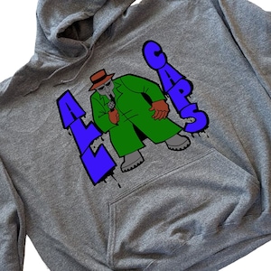 Op de afbeelding: Grijs hoodie met een grafische print van een cartoonfiguur dat een groene jas en een hoed draagt en een microfoon vasthoudt. De tekst "LA CARS" is in blauw en paars gedrukt.
