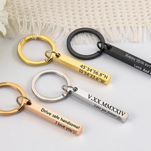 May include: Three gold, silver, and black keychains with engraved bars. The gold bar reads "45°34'56.8"N 10°54'33.6"W". The silver bar reads "V.XX.MMXXIV Love you forever". The black bar reads "Happy 18th birthday Love dad xxx".