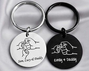 May include: Two silver keychains with round black and white engraved tags. The white tag has the text "Sam, Lucy & Daddy" and the black tag has the text "Emily & Daddy". Both tags feature a design of three fists bumping together.