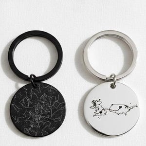 May include: Two keyrings with circular pendants. One is black with a constellation design, the other is white with a cow illustration and a map. Both have metal key rings.