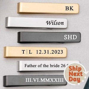 Könnte beinhalten: Sechs Krawattenklammern in Gold, Silber und Schwarz mit graviertem Text. Der Text auf den Krawattenklammern lautet: "BK", "Wilson", "SHD", "T|L 12.31.2023", "Father of the bride 26" und "III.VI.MMXXIII".