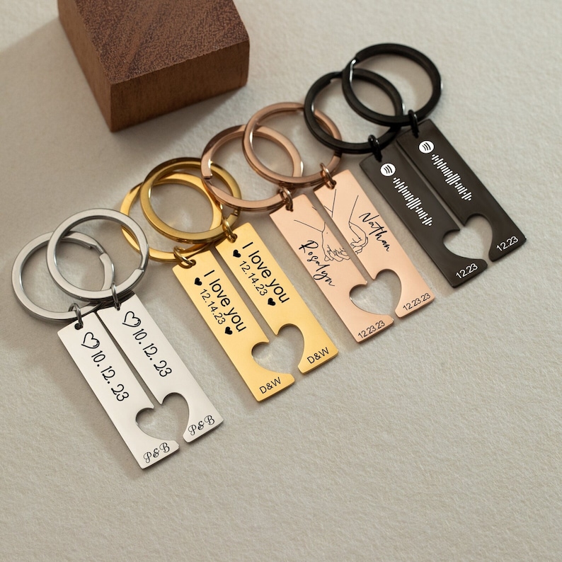 May include: Set of five matching couples' keychains with heart-shaped cutouts. Each keychain features a personalized inscription with names, dates, and the phrase "I love you". The keychains are made of metal and come in silver, gold, and rose gold.