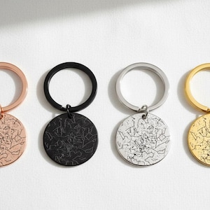 Op de afbeelding: Vier sleutelhangers in roségoud, zwart, zilver en goud. Elke sleutelhanger heeft een ronde hanger met een gedetailleerd kaartontwerp. De sleutelringen zijn cirkelvormig en de hangers zijn met een kleine lus bevestigd.