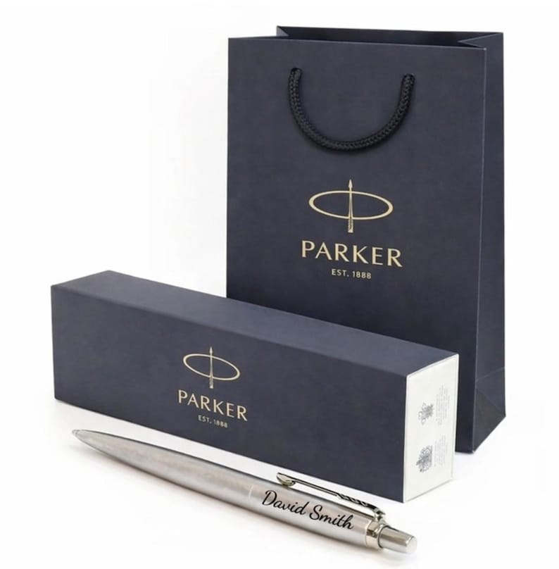 May include: A silver pen with the name "David Smith" engraved on the side, presented with a navy blue gift box and matching shopping bag. The box and bag feature the "PARKER" logo in gold.