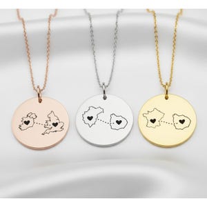 Puede incluir: Tres collares con colgantes redondos. Los colgantes son de oro rosa, plata y oro. Cada colgante presenta el contorno de dos lugares conectados por una línea de puntos y un símbolo de corazón.