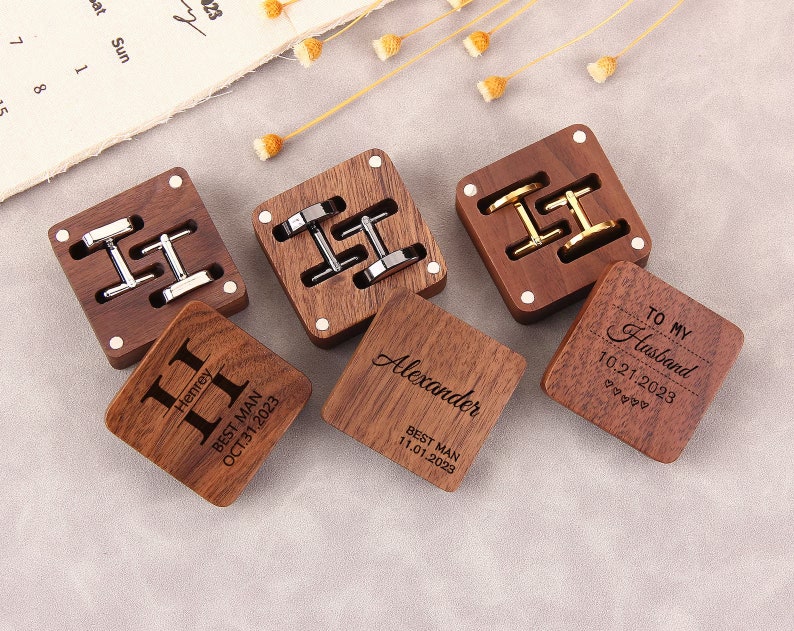 May include: Four wooden boxes with engraved text and cufflinks inside. The boxes are made of dark wood and have a polished finish. The text on the boxes includes "Best Man", "To My Husband", "Alexander", and "Henrey". The cufflinks are silver and gold.